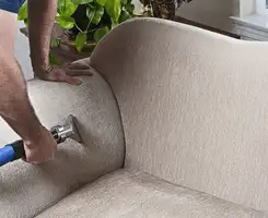 Professional upholstery cleaner deep-cleaning a fabric sofa with a handheld extraction tool and hose in Jacksonville, FL.
